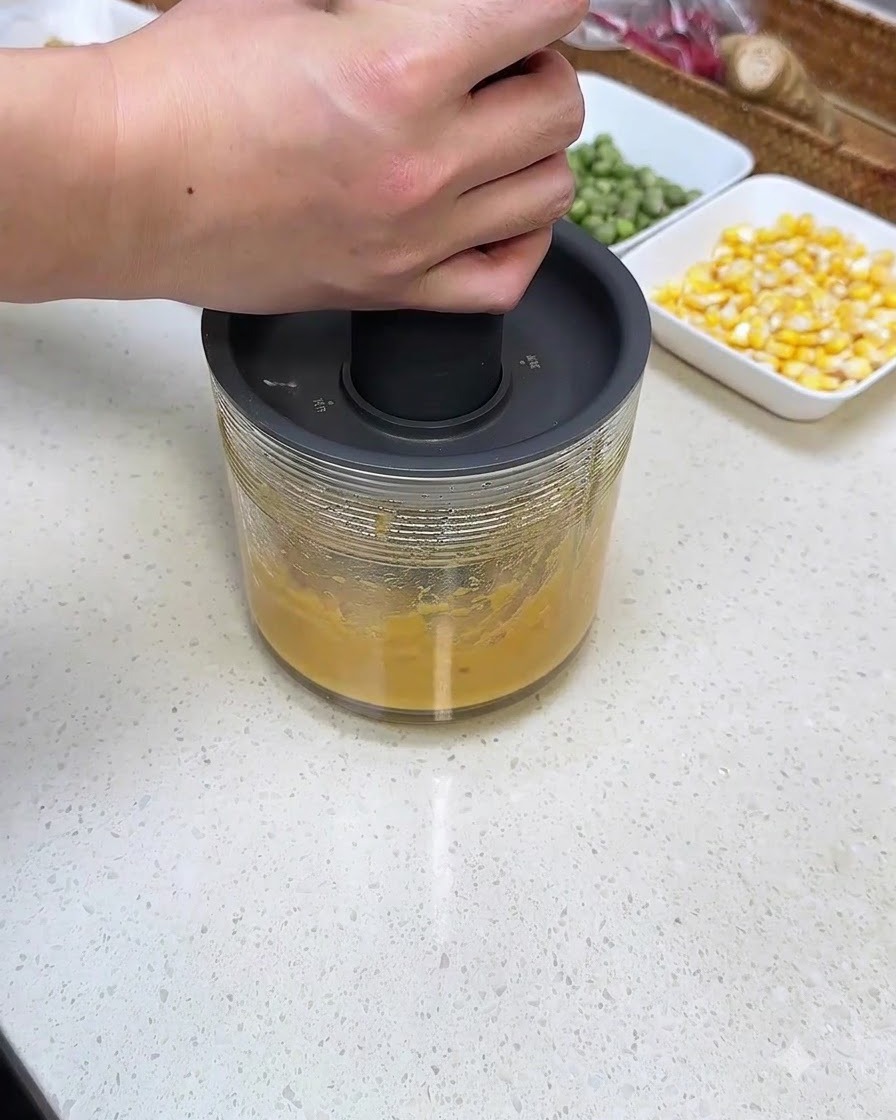 Una persona presionando una licuadora de mano sobre un recipiente de vidrio lleno de puré de batata.