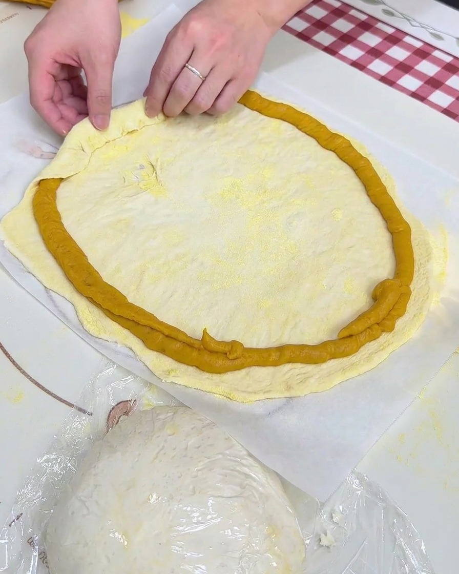 Manos doblando el borde de la masa sobre el anillo de puré de batata aplicado sobre papel pergamino.