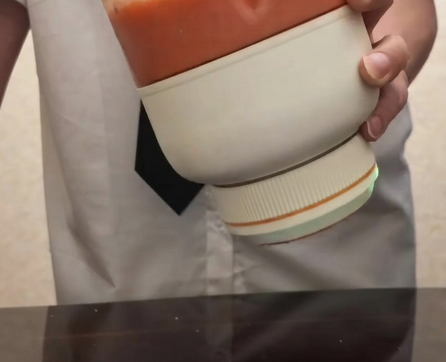 Una persona sosteniendo una licuadora eléctrica portátil llena de puré de tomate rojo brillante y suave.
