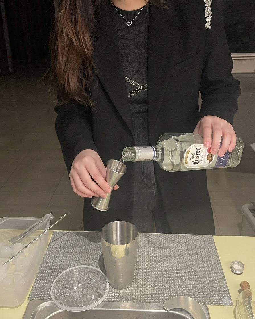 Tequila siendo vertido de una botella a un medidor sobre una coctelera de metal.