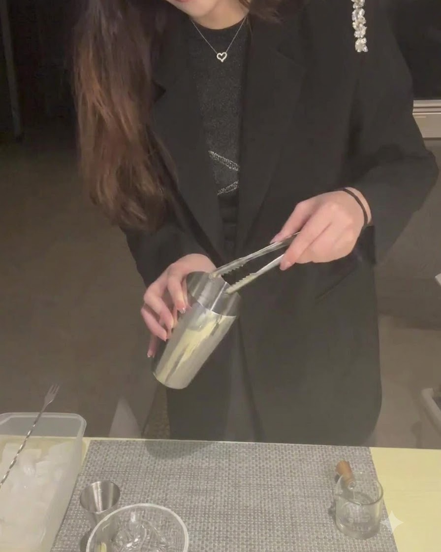 Una persona usando pinzas para colocar cubitos de hielo en una coctelera de metal.