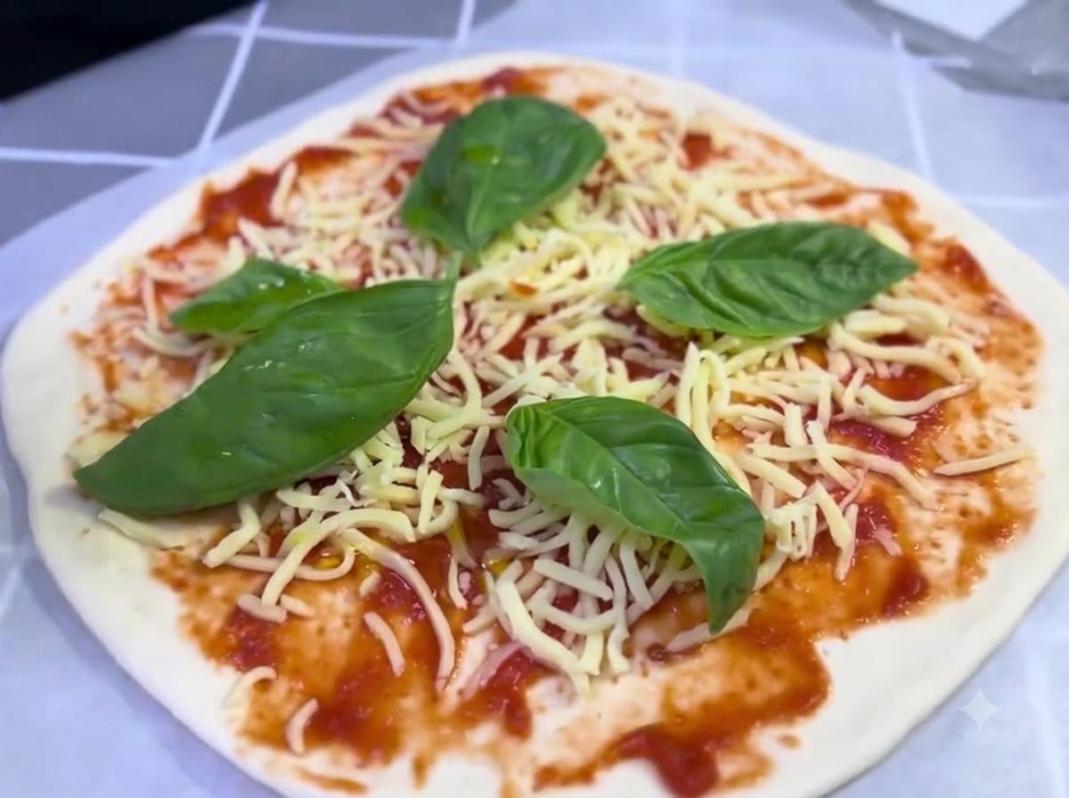 Una pizza armada cubierta con queso y hojas de albahaca recibiendo un ligero chorrito de aceite de oliva.