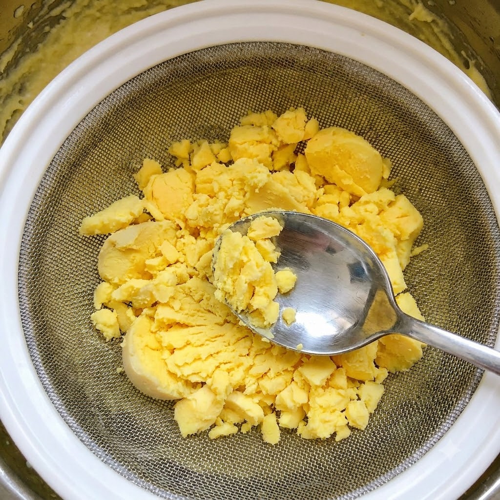 Tamizando yemas de huevo cocidas a través de un colador de malla metálica usando una cuchara.