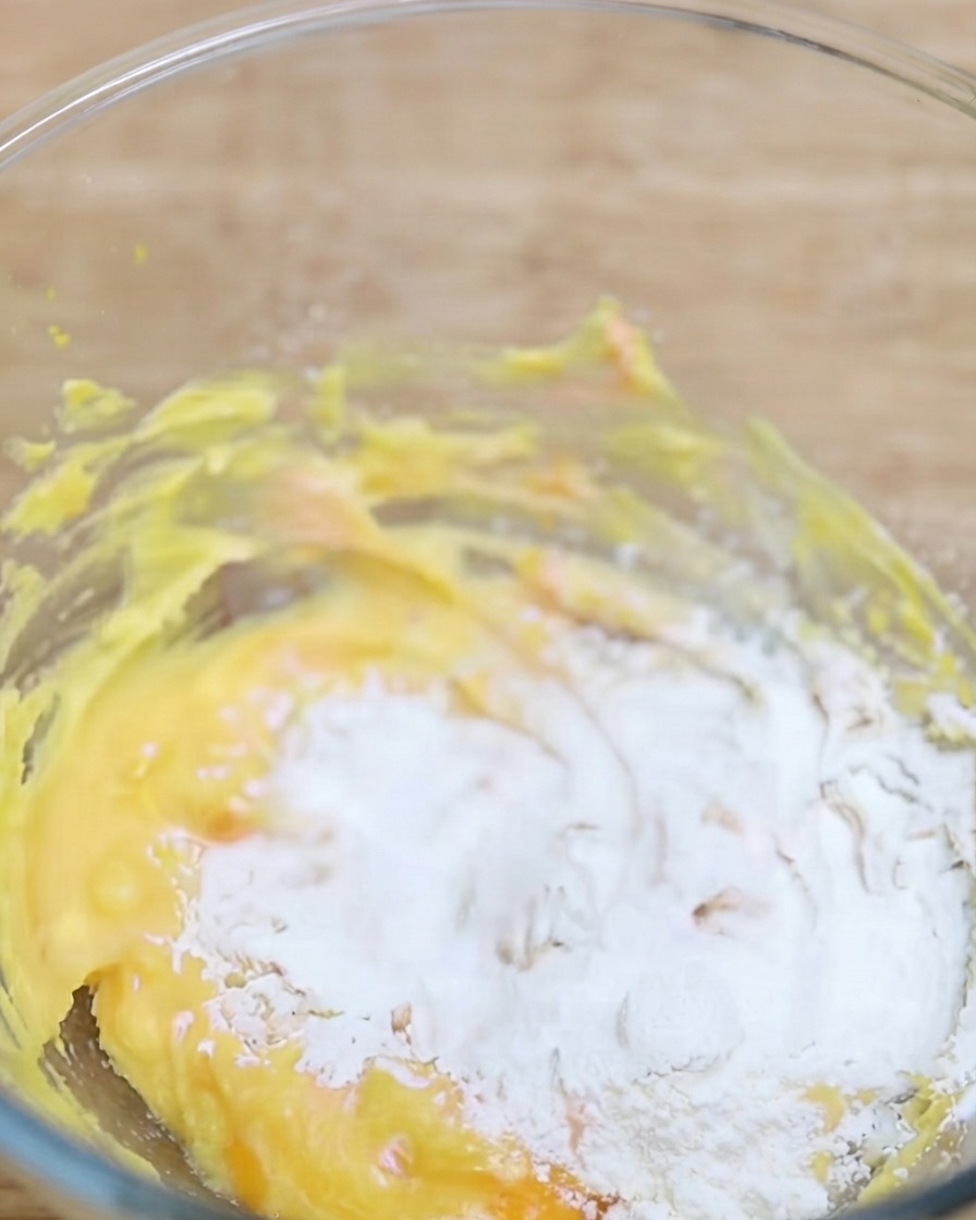 Polvo de matcha siendo tamizado en un tazón que contiene la base de masa amarilla.