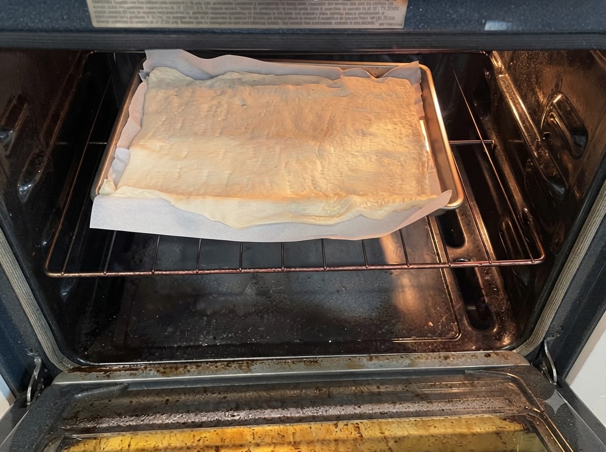 Una bandeja de horno con masa de pizza cruda sobre papel de horno colocada en la rejilla dentro de un horno precalentado.