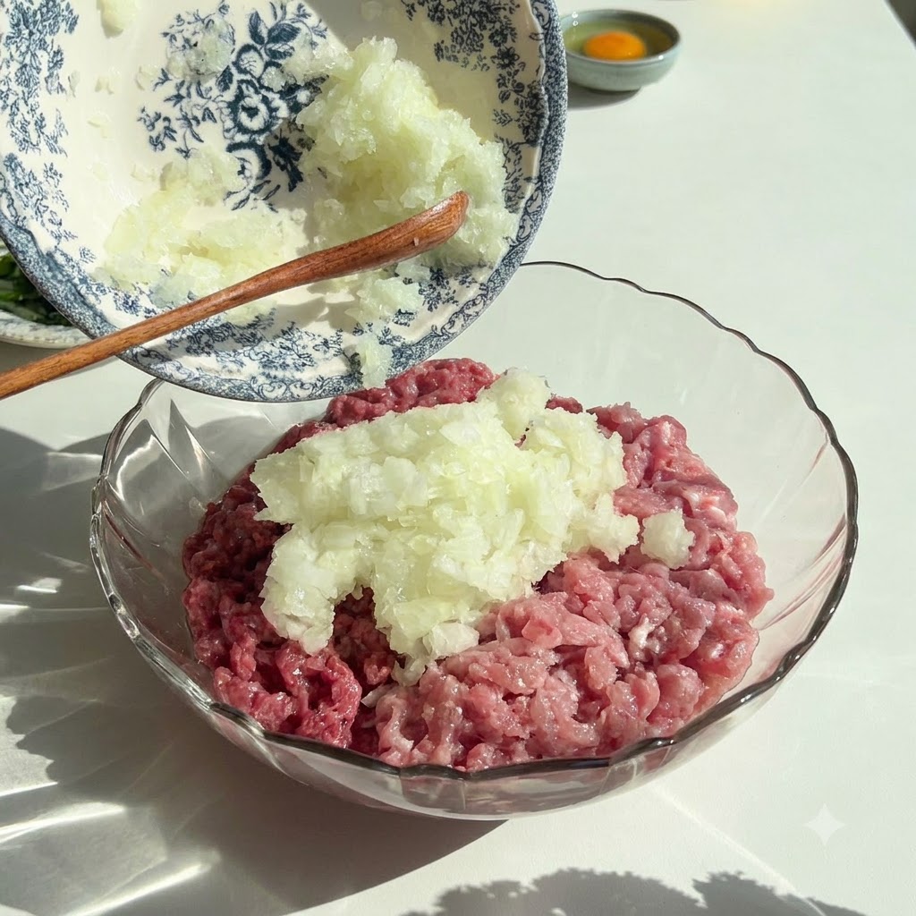 Cebollas y perejil finamente picados vertidos desde un bol decorativo en un bol de vidrio que contiene carne picada cruda.