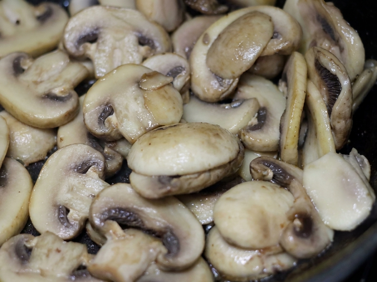 Champiñones blancos en rodajas chisporroteando y cocinándose en una sartén con crema ligera.