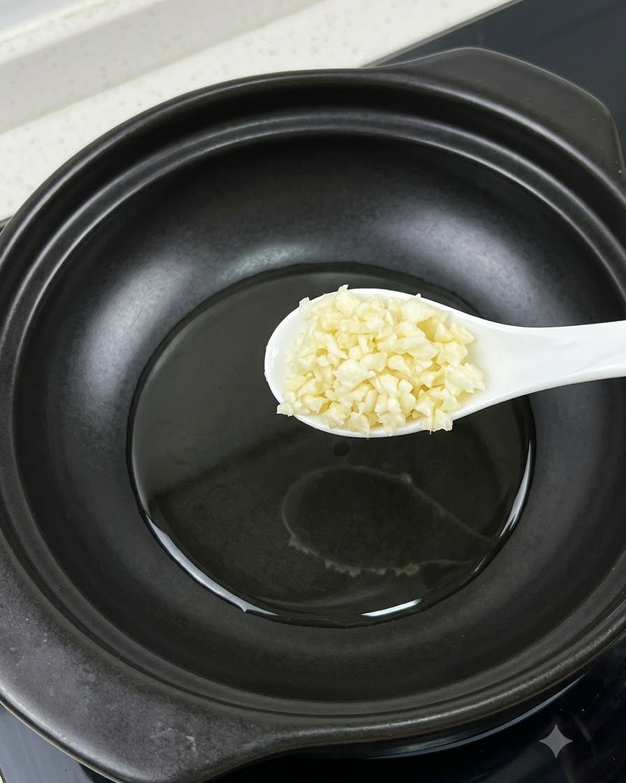 Una cuchara de ajo picado sostenida sobre una olla junto a una yema de huevo separada.
