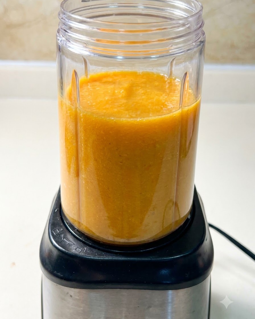 Un vaso de licuadora lleno de una mezcla de sopa anaranjada sentado sobre una base de motor de licuadora negra.