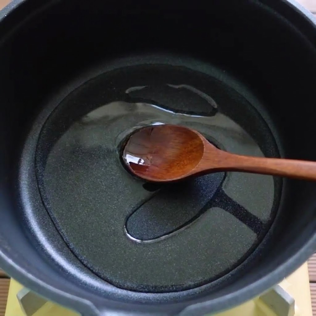 Una cuchara de madera revolviendo aceite e ingredientes derretidos en una olla negra.