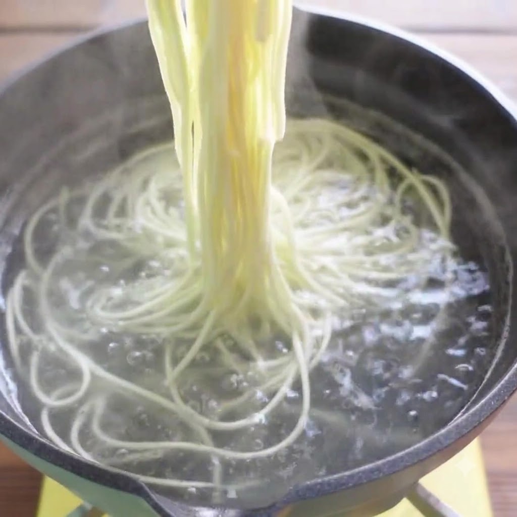 Palillos levantando fideos de ramen cocidos fuera del agua hirviendo.