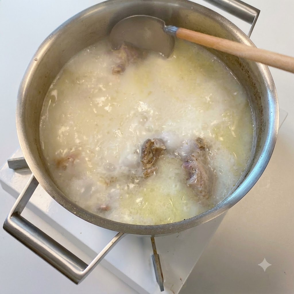 Un cucharón de madera sumergiéndose en una olla de caldo de hueso de cerdo opaco y lechoso.