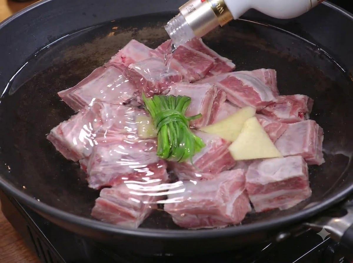 Trozos de carne siendo colocados en una olla con agua, cebollinos y jengibre para blanquear.