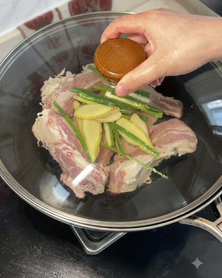 Una mano sosteniendo una tapa o vertiendo vino amarillo sobre las costillas de res, el jengibre y los cebollinos en un wok.