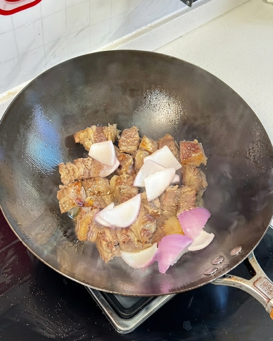 Trozos de costilla de res salteados en un wok mezclados con trozos de cebolla y salsas de soja.
