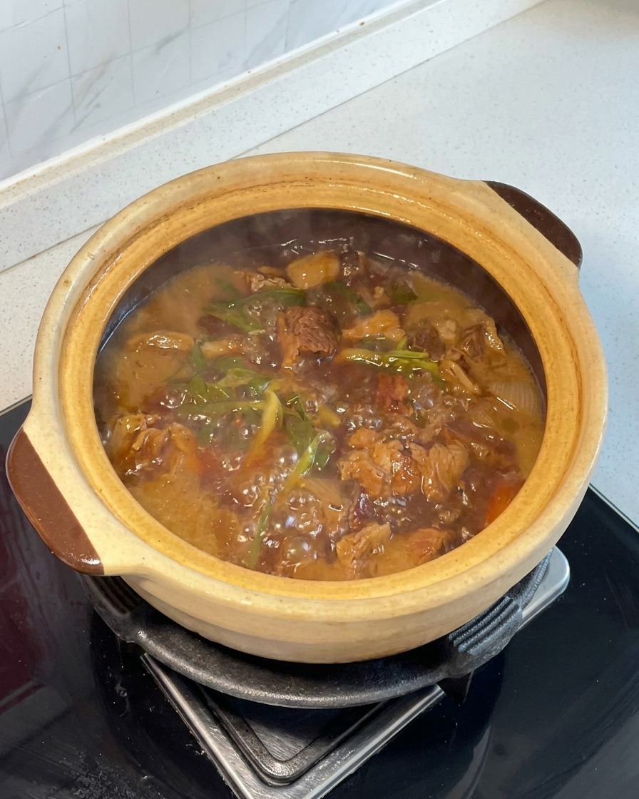 Trozo de patatas y zanahorias mezclados en la carne estofada al estilo rojo dentro de una cazuela de barro.