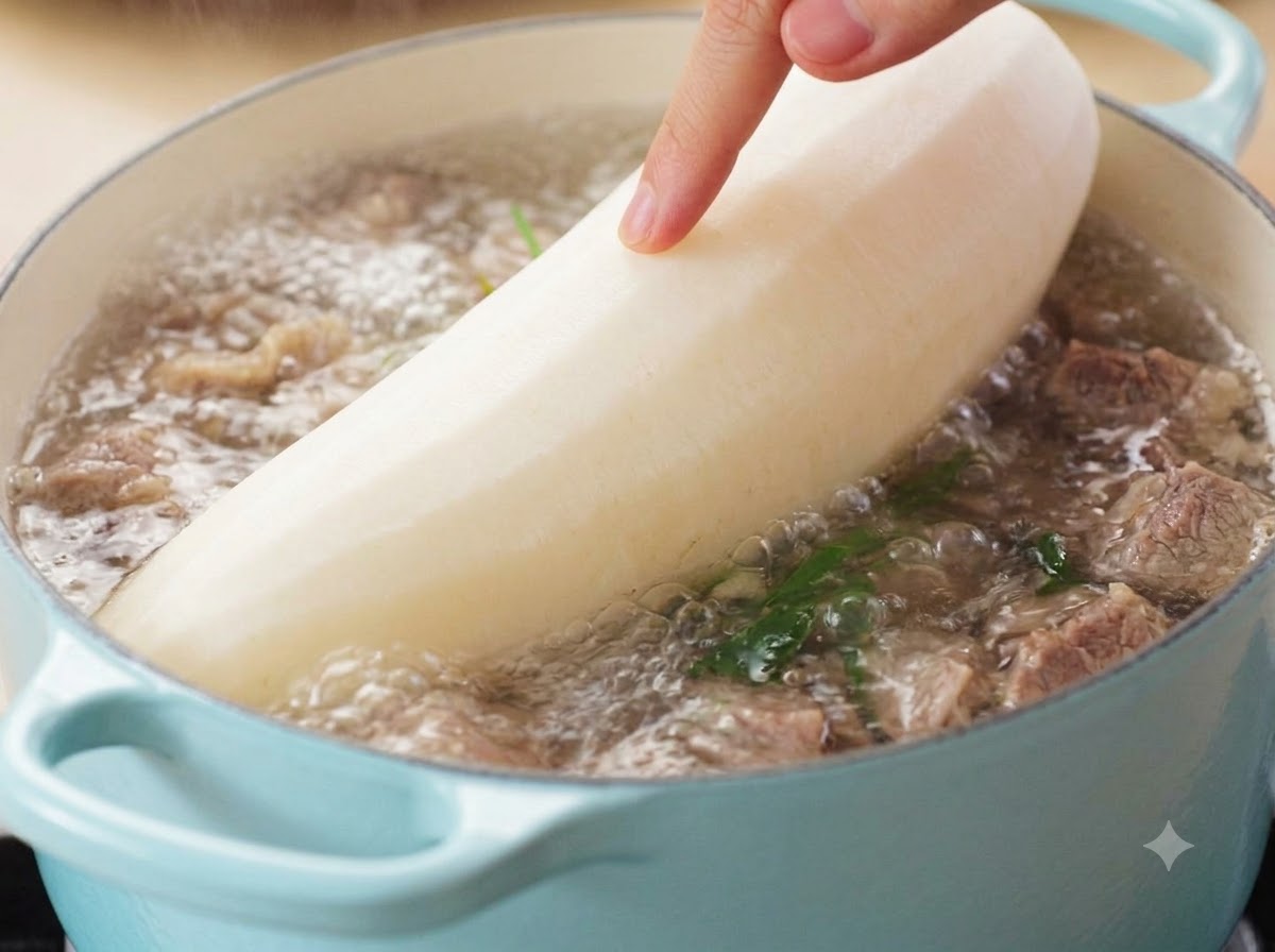 Una mano guiando un rábano blanco grande pelado hacia una olla burbujeante de sopa de res.