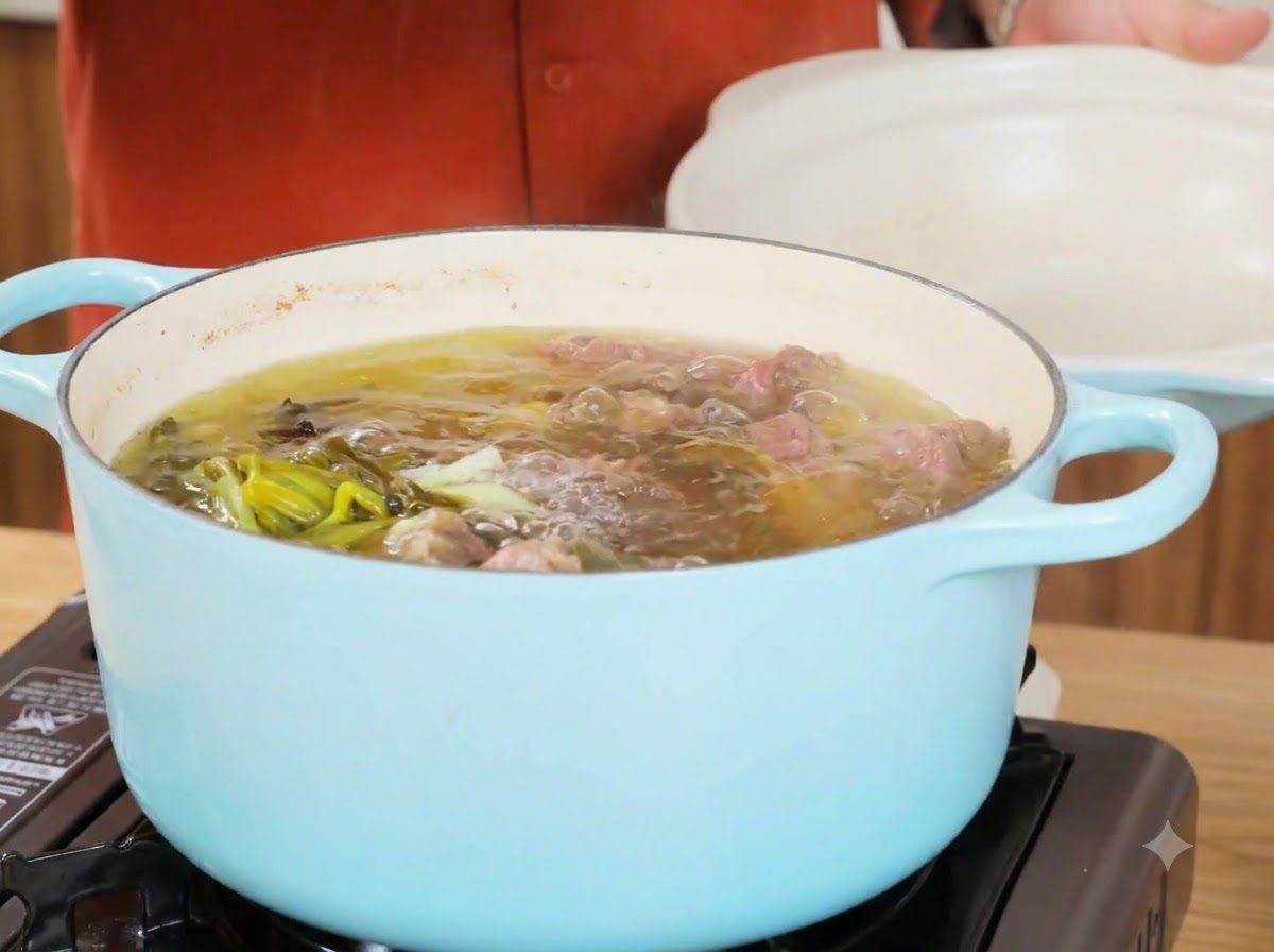 Una olla de caldo de res hirviendo a fuego lento después de retirar los ingredientes principales, mostrando líquido claro y cebollas verdes.