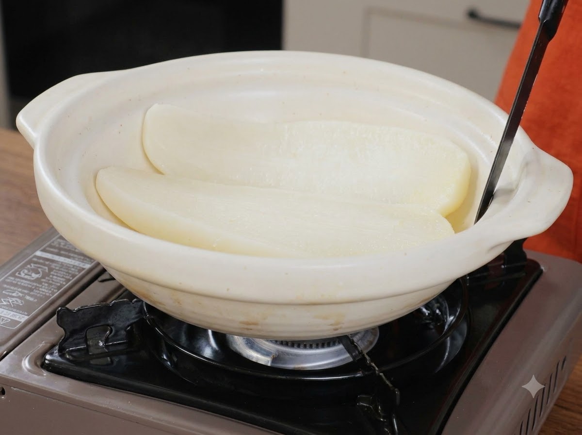Dos mitades de rábano blanco cocido descansando dentro de una olla de servicio de cerámica blanca ancha con un utensilio.