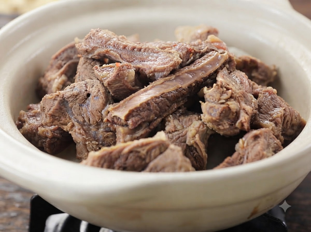 Una vista de cerca de trozos tiernos de costilla de res cocidos amontonados dentro de un plato de cerámica blanca.