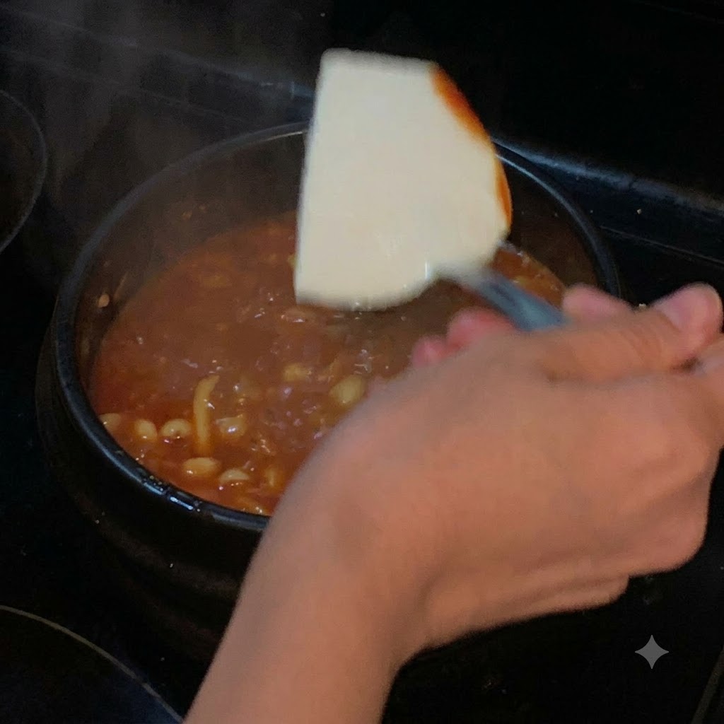 Un bloque de tofu suave introduciéndose con una espátula en una olla de sopa roja hirviendo a fuego lento.