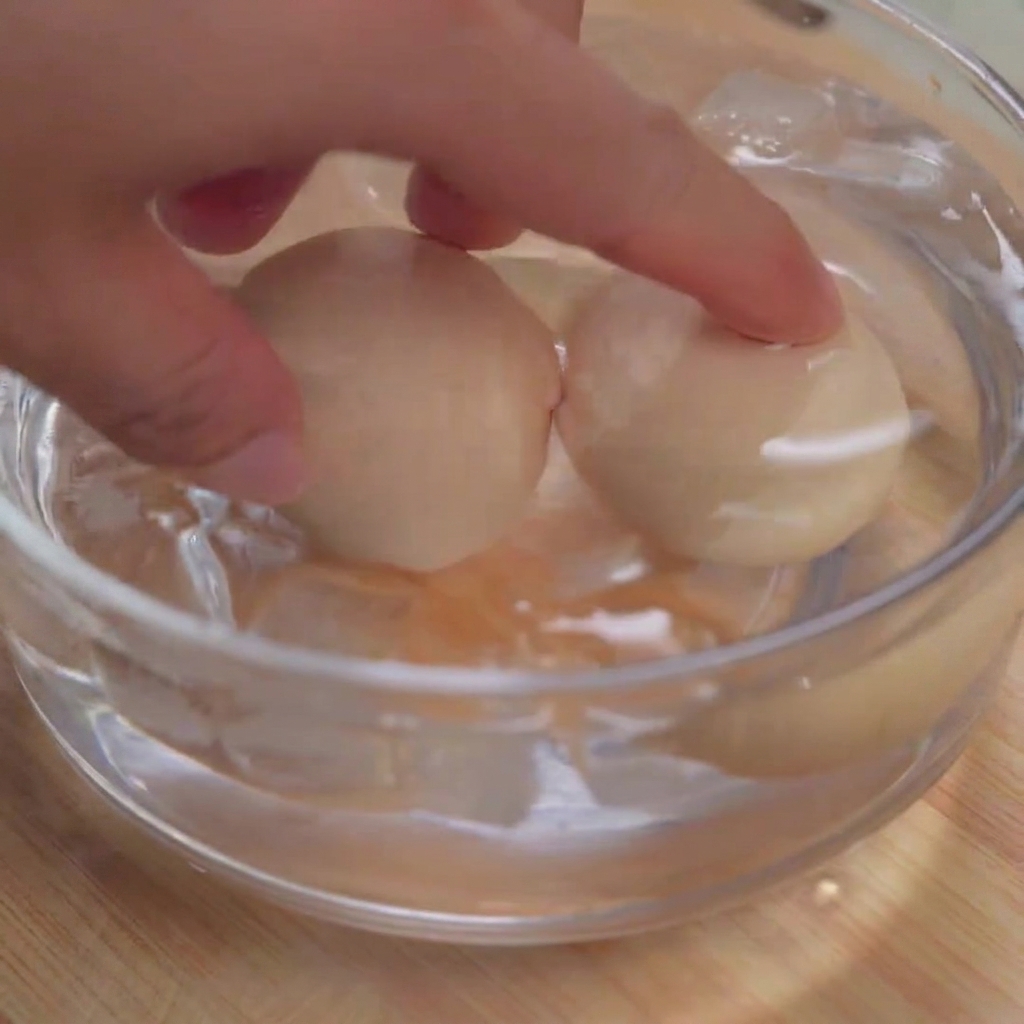 Dos huevos pasados por agua sumergidos en un cuenco de vidrio transparente lleno de cubitos de hielo y agua fría.