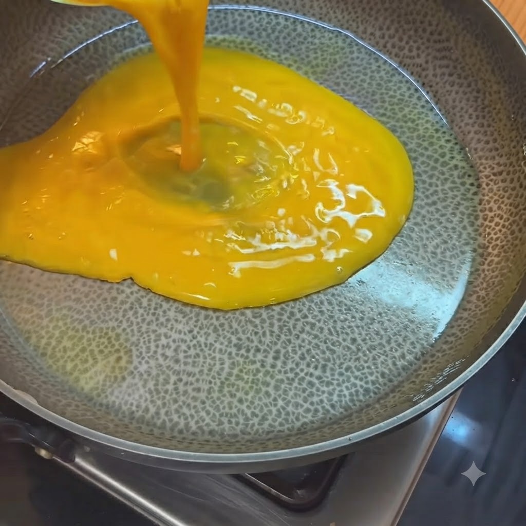 Huevos batidos de color amarillo brillante vertidos desde una taza medidora en un sartén caliente con aceite.