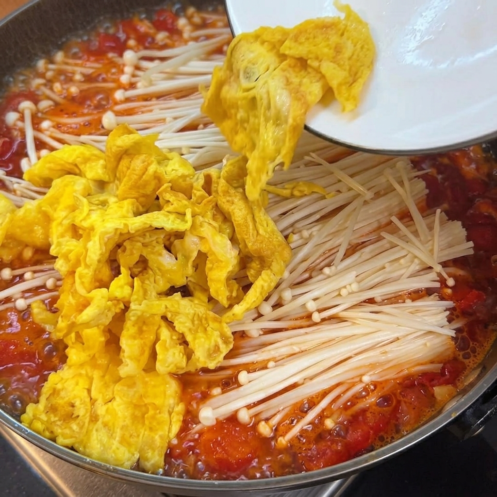 Cubos de tofú tierno siendo añadidos a la olla que contiene el caldo de tomate, los hongos y los huevos.