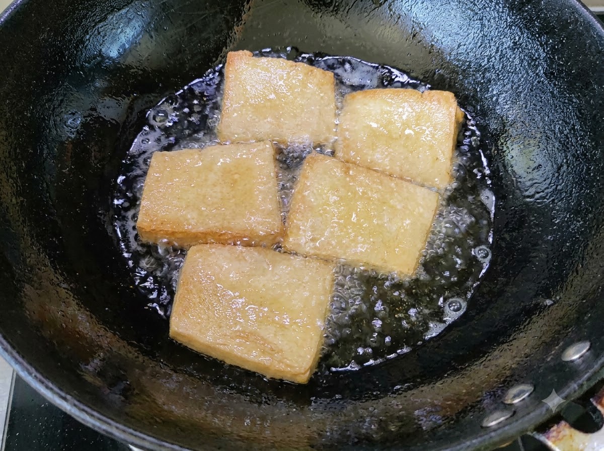 Trozos de tofu dorado friéndose en un wok con aceite burbujeante.