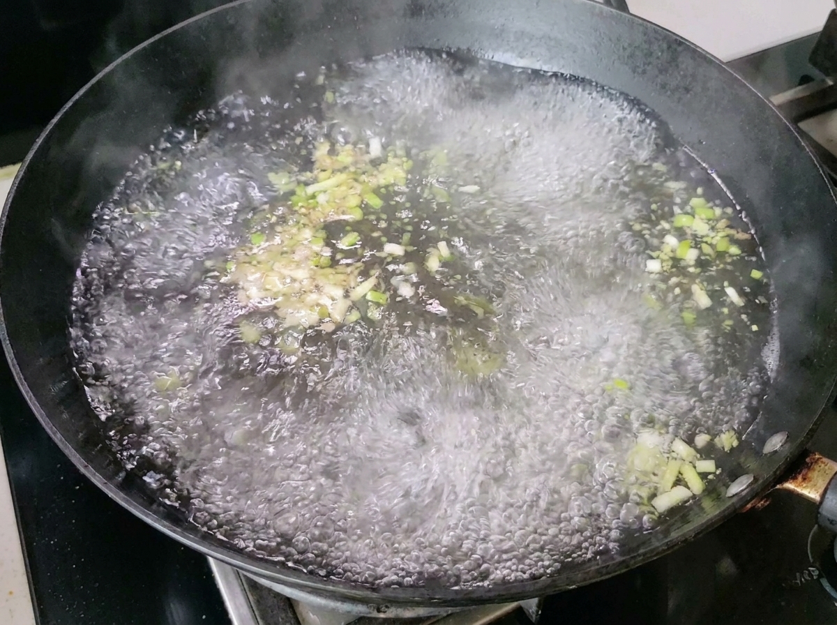 Agua hirviendo con cebollinos y jengibre produciendo vapor en el wok.
