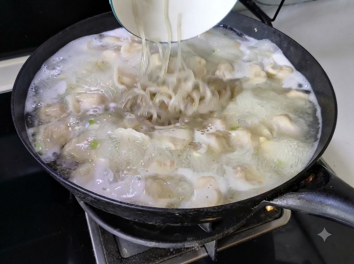 Fideos siendo vertidos desde un bol blanco en la sopa de dumplings burbujeante dentro de un wok.