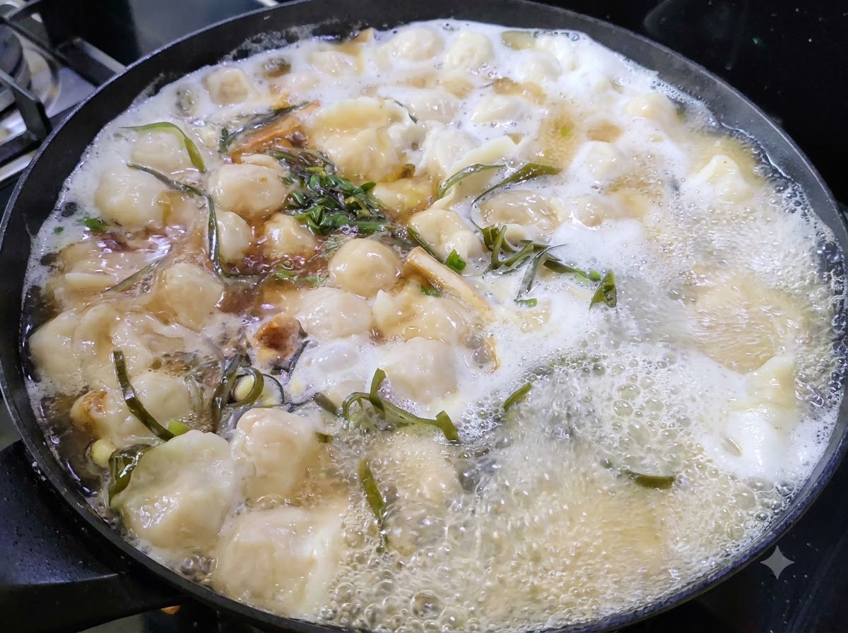 Hierbas verdes picadas flotando en la superficie de una olla humeante de sopa de dumplings.