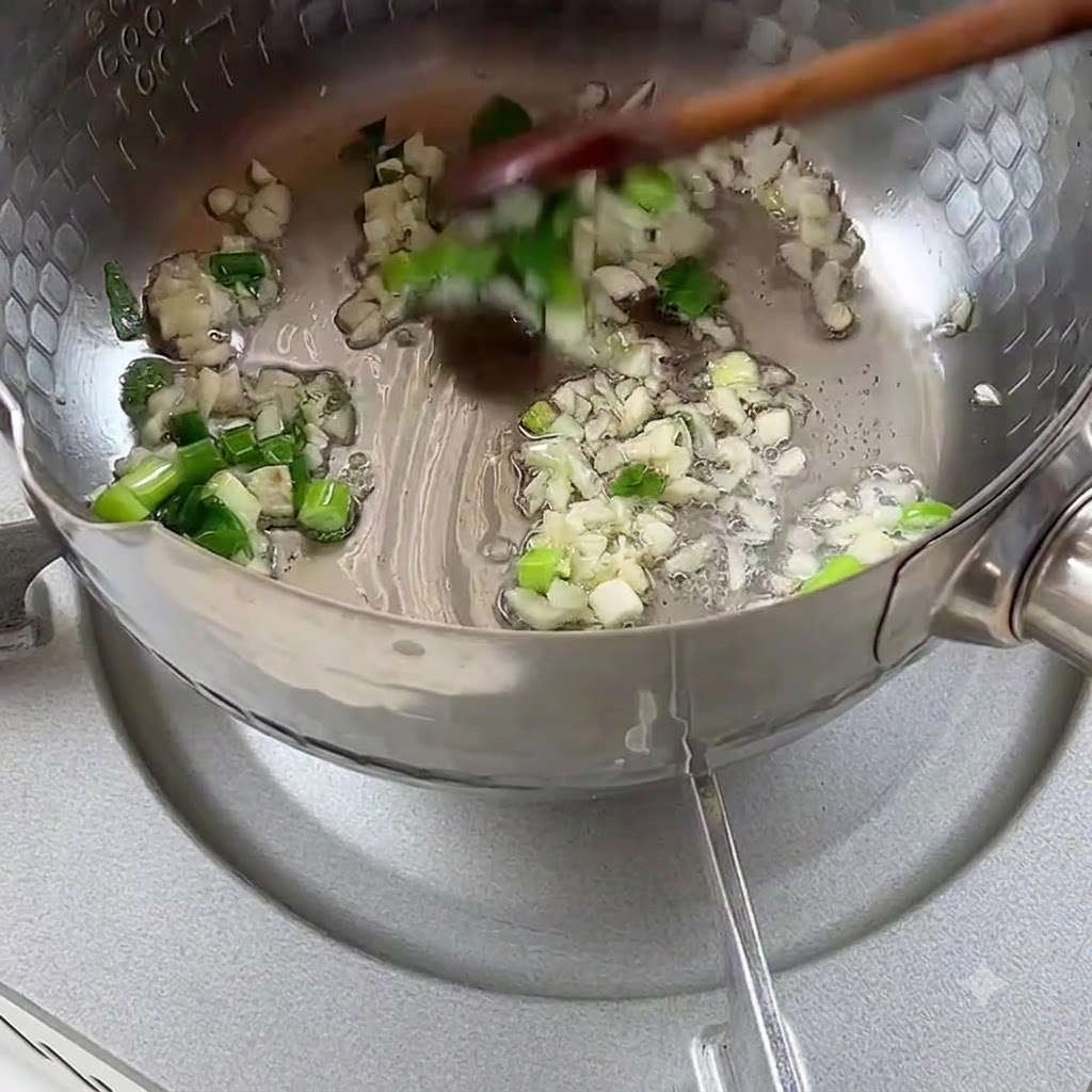 Cebolleta picada y ajo dorándose en aceite dentro de una olla de metal.