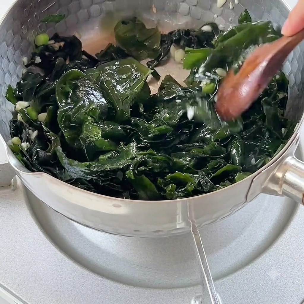 Agua hirviendo vertiéndose en una olla llena de algas y aromáticos salteados.