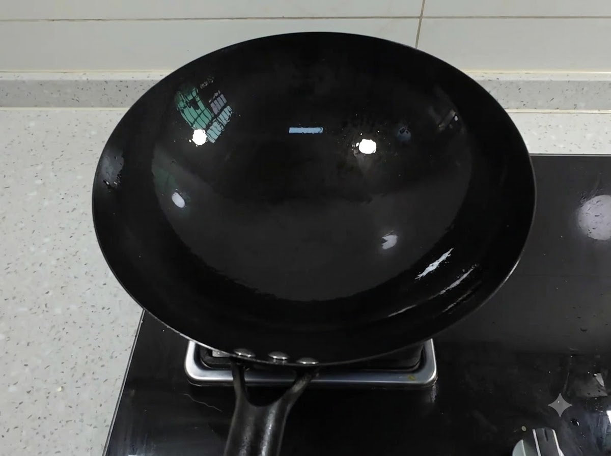 Un wok de hierro negro limpio sobre el quemador de una estufa de gas con aceite acumulándose en su interior.