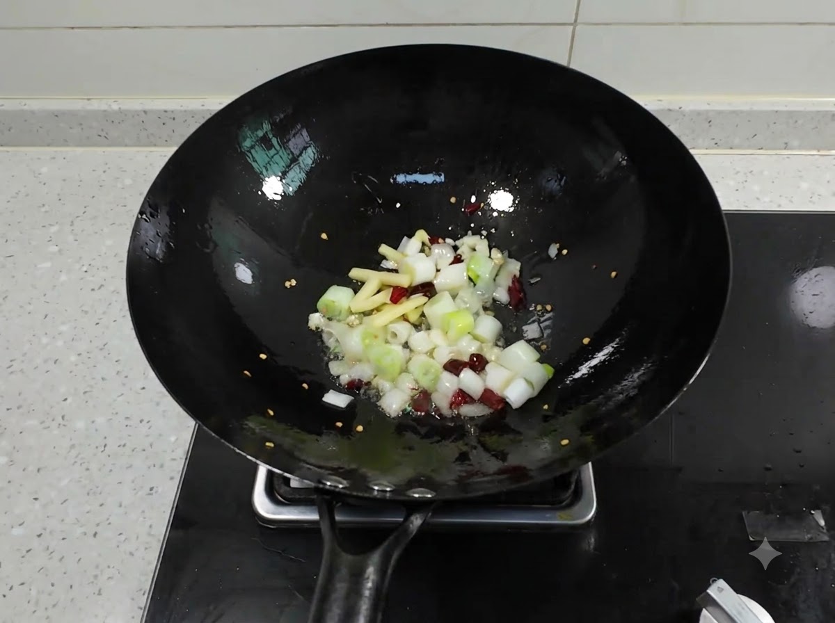 Cebollines picados, jengibre, ajo y chiles secos chisporroteando en un wok negro con aceite caliente.
