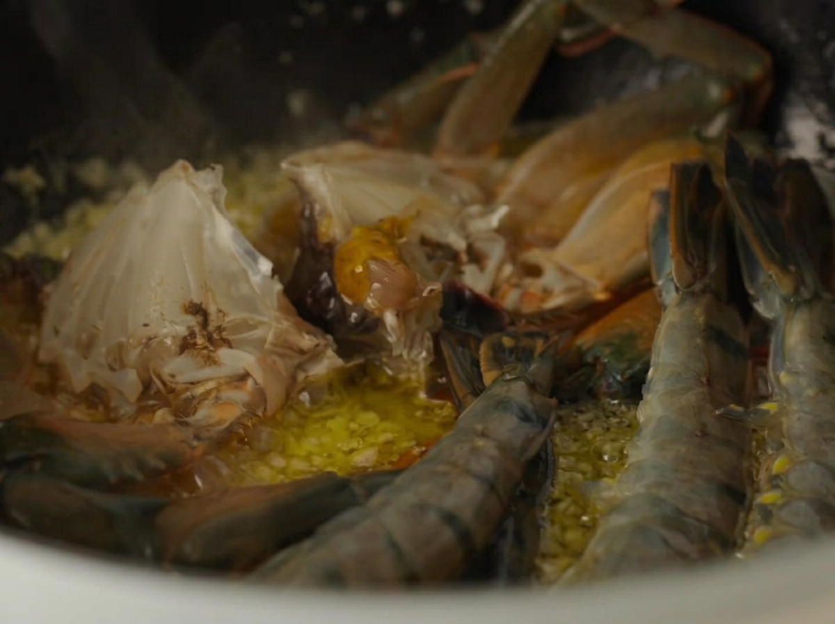 Partes de cangrejo crudo y camarones crudos cocinándose dentro de una olla con mantequilla de ajo.