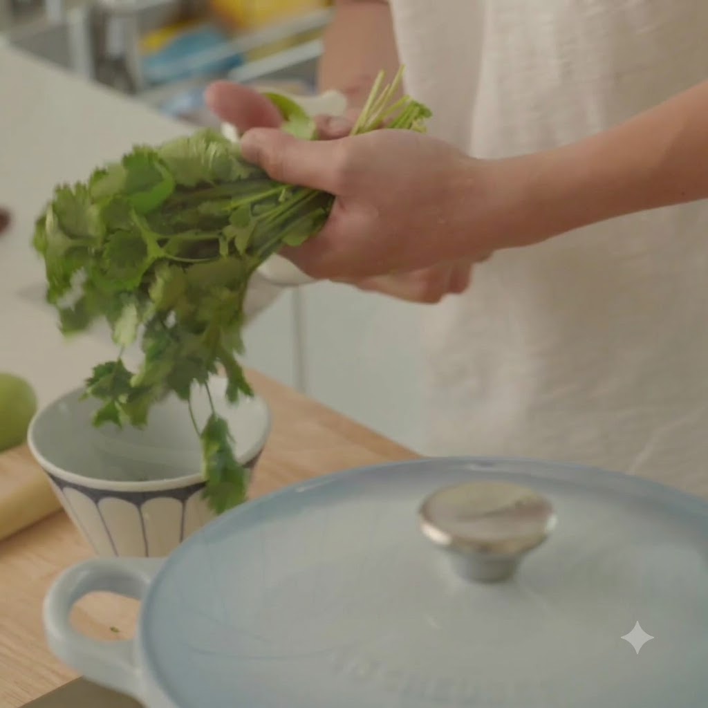Cilantro fresco siendo preparado y picado cerca de un tazón y una olla de cocina.
