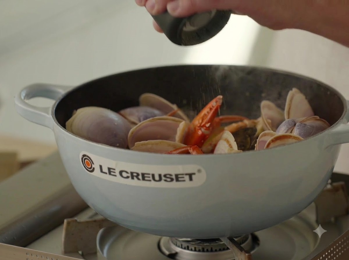 Pimienta negra fresca siendo molida sobre el caldo de mariscos burbujeante en una olla.