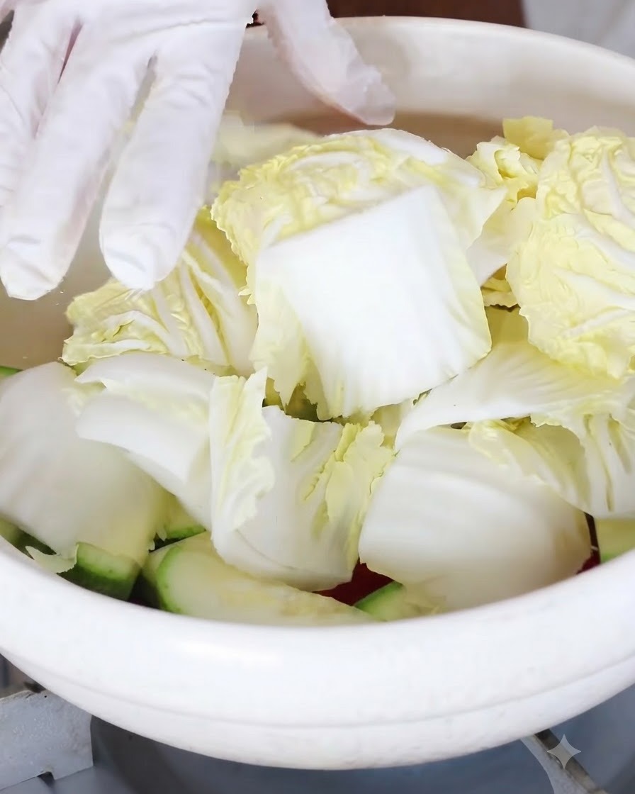 Trozos de repollo tierno siendo añadidos encima de las verduras en la olla.