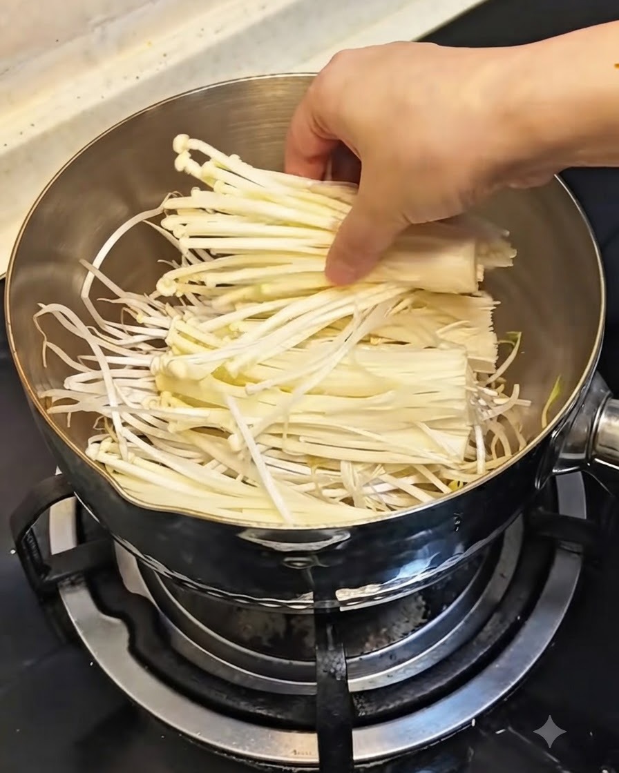 Una mano colocando un atado de setas enoki blancas frescas sobre los brotes de soja en la olla.