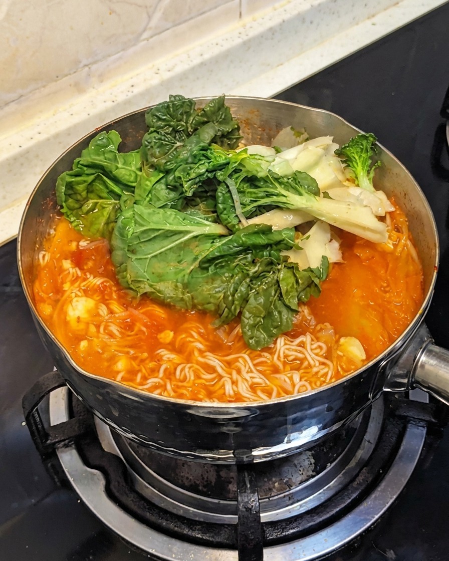 Verduras de hoja verde frescas añadidas sobre los ingredientes hirviendo en la olla.