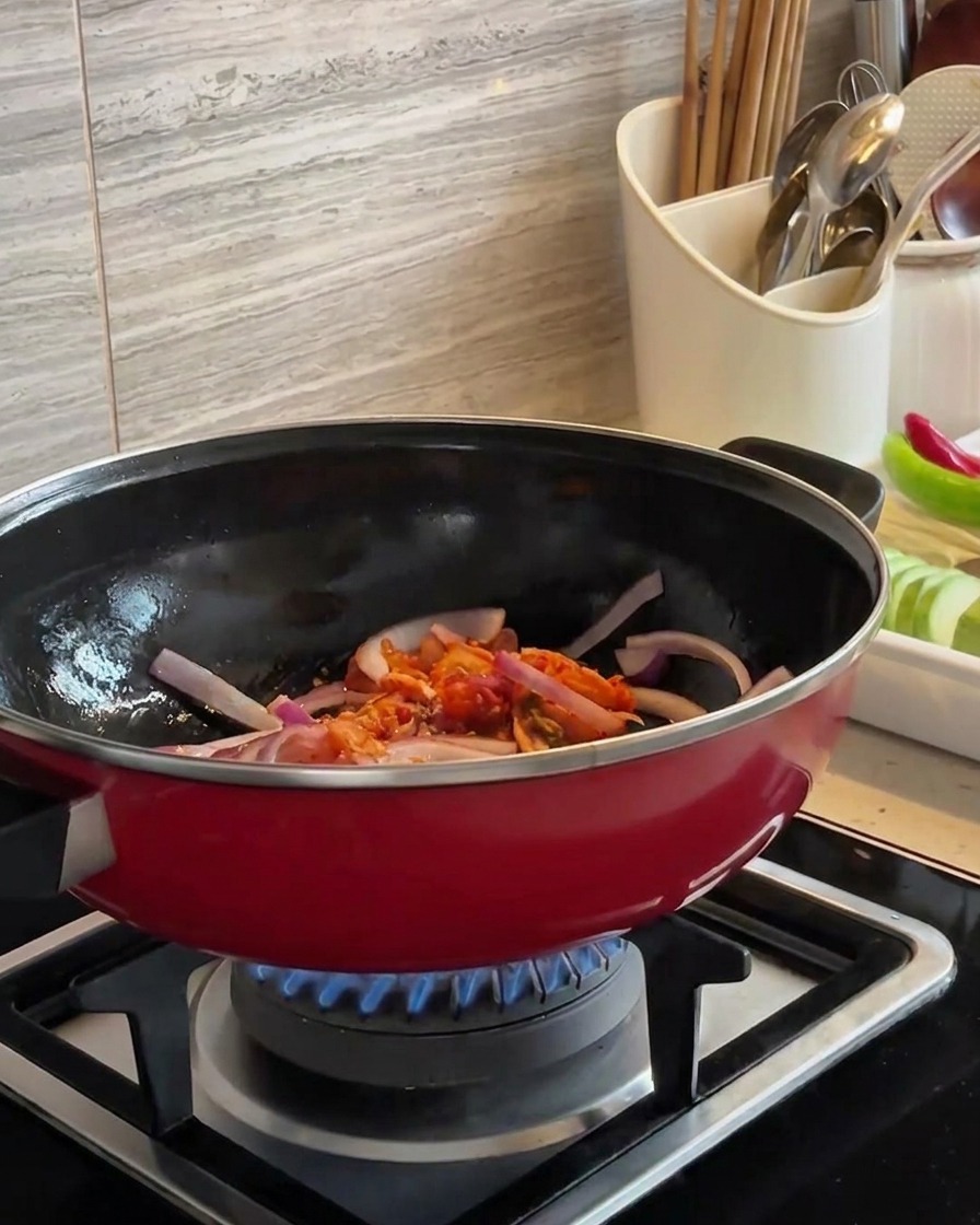 Rodajas de cebolla roja y kimchi picado siendo salteados juntos en un wok rojo sobre una llama azul.