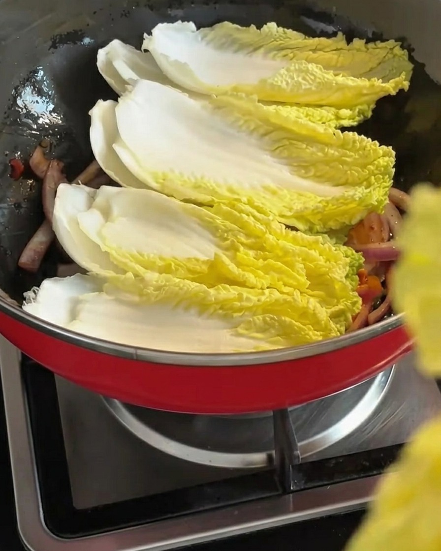 Hojas de col napa frescas siendo colocadas sobre la mezcla de cebolla salteada y kimchi.