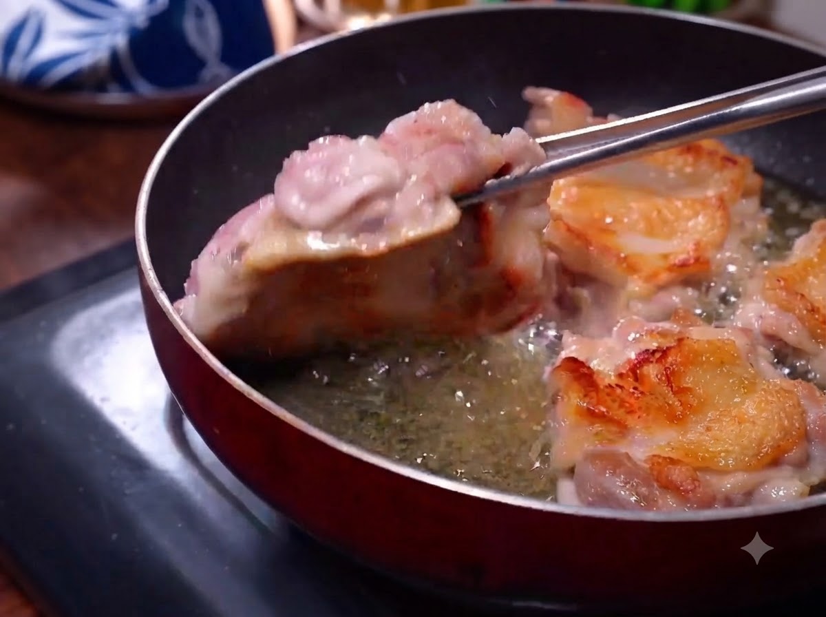 Muslos de pollo friéndose en una sartén con piel dorada visible mientras unas pinzas los voltean.