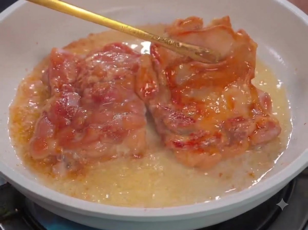 Pinzas de cocina volteando trozos de pollo en una sartén blanca con aceite.