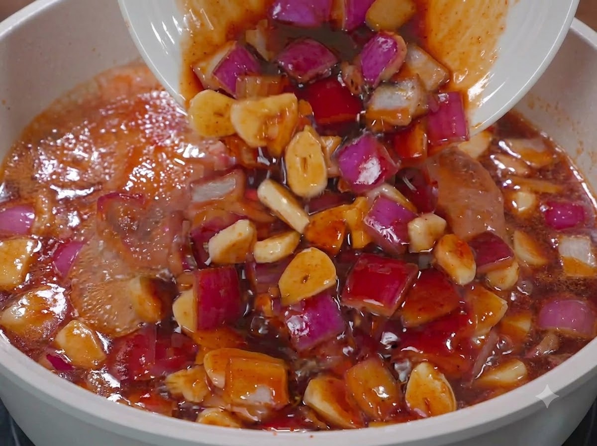 Salsa y cebollas rojas siendo vertidas desde un plato blanco en una sartén con pollo.