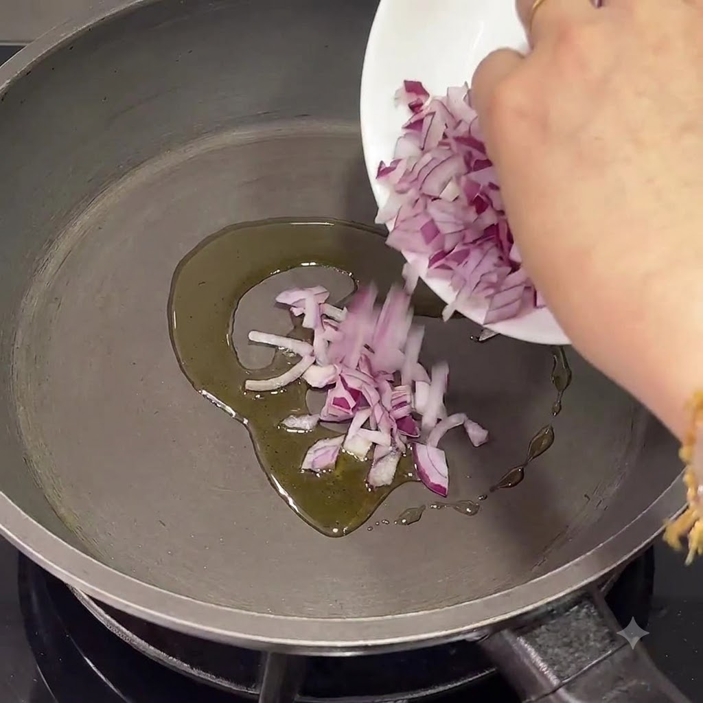 Cebollas moradas picadas siendo vertidas en una sartén con aceite de oliva tibio.