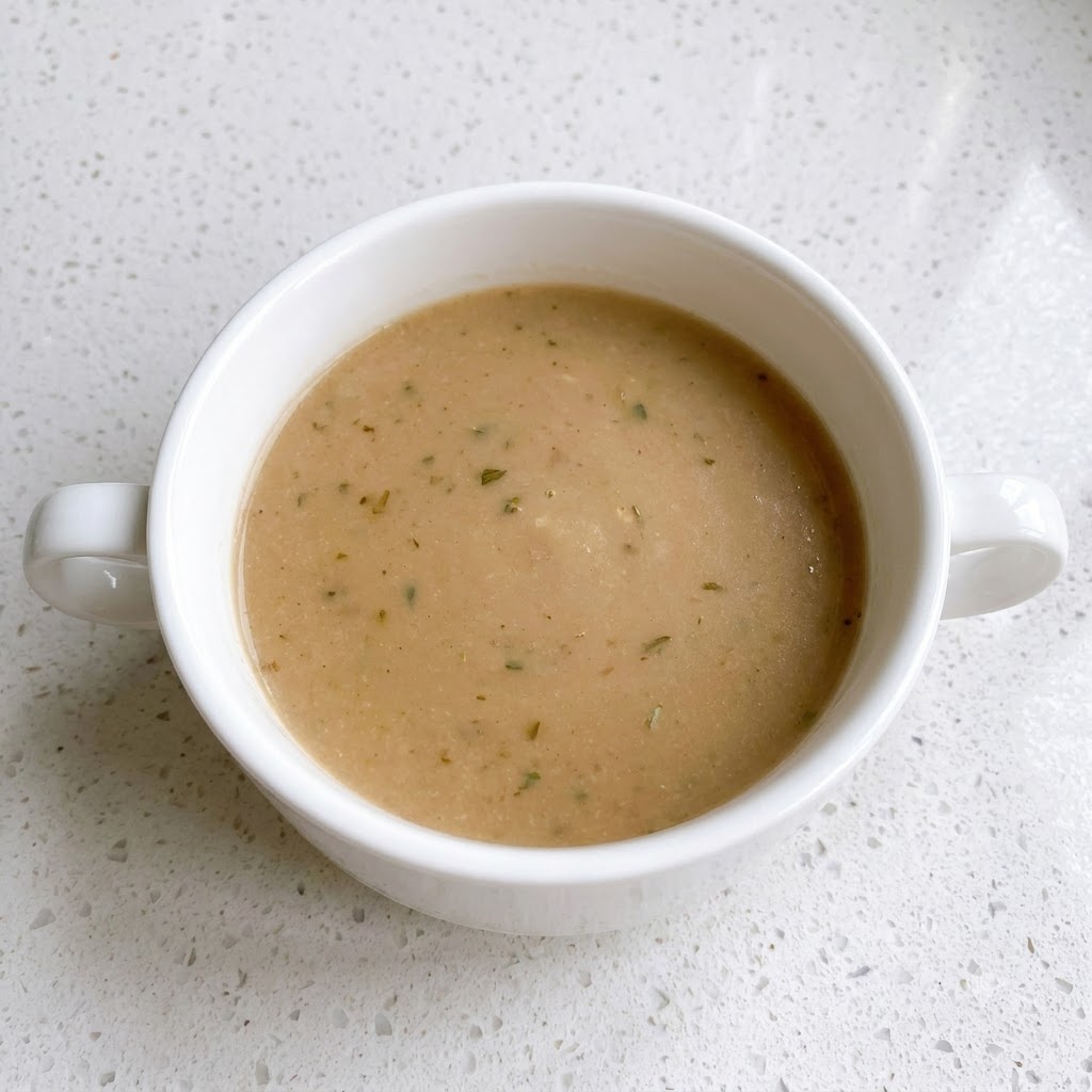 Un tazón blanco que contiene una mezcla de salsa marrón mezclada con motas de pimienta.