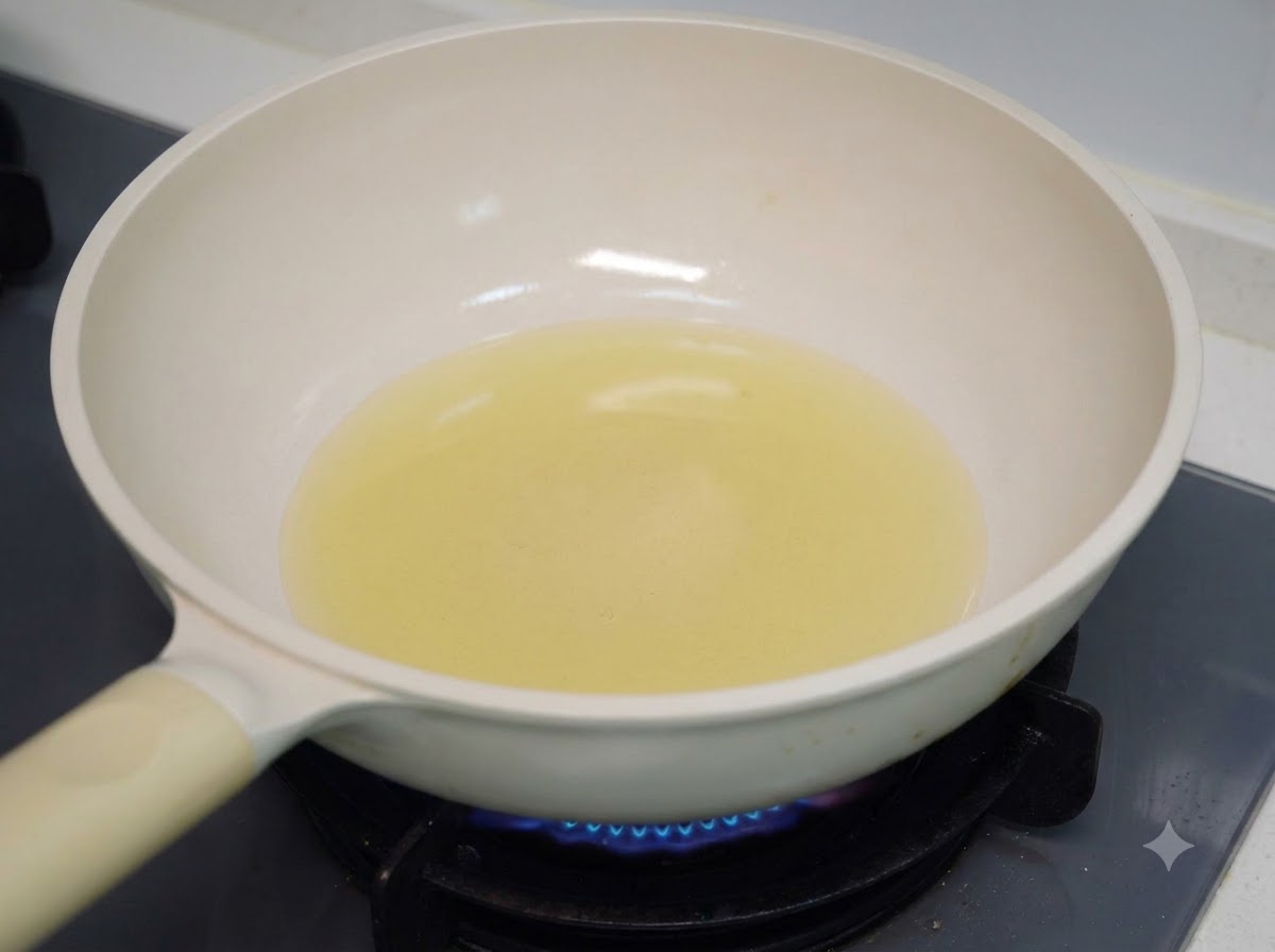 Aceite de cocina calentándose en una sartén blanca sobre una hornalla de gas.